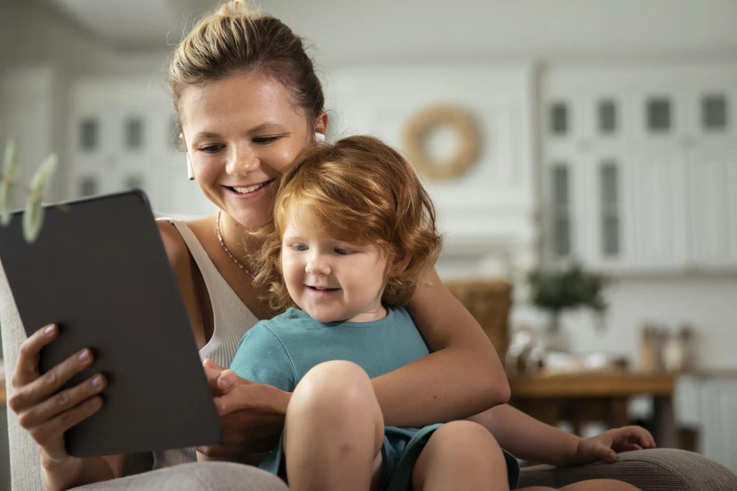 Mãe com filho no colo, ambos sorrindo para um tablet e usando aplicativos