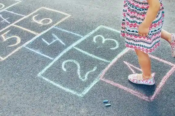 Brincadeiras de antigamente. Criança brincando de amarelinha, desenhada com giz no chão.