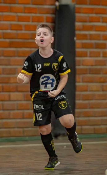 Bernardo, ex-paciente oncológico, em meio a um jogo de futsal, sorrindo e comemorando. Novembro Dourado.