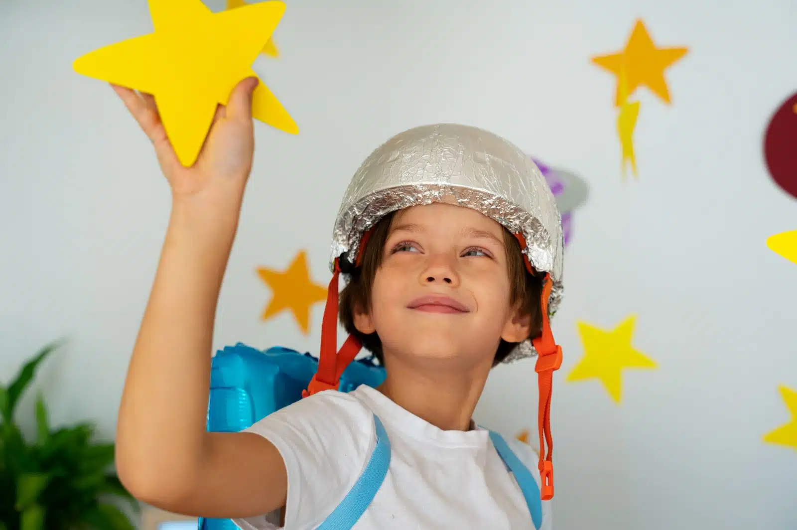 Menino brincando de astronauta, com muita imaginação, um capacete de alumínio e estrelas de papel